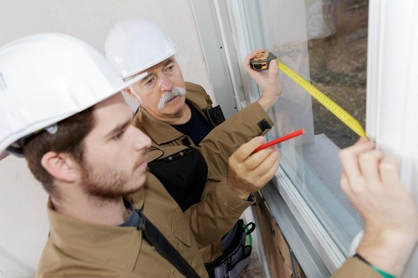 На фото – строители измеряют ширину окна