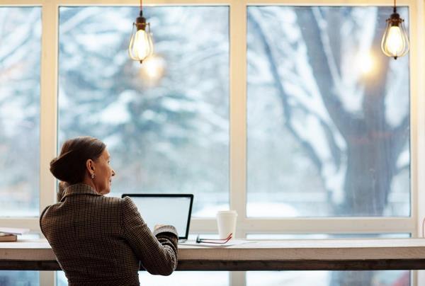 На фото – женщина с ноутбуком возле окна