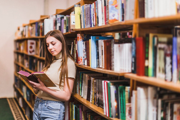 Девушка читает книгу в библиотеке